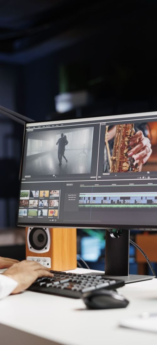 Man working with video footage and sound Male cinematographer working with footage and sound, editing new project, cutting film montage seated at office desk. Detailed view of man using computer processing movie in post production software.